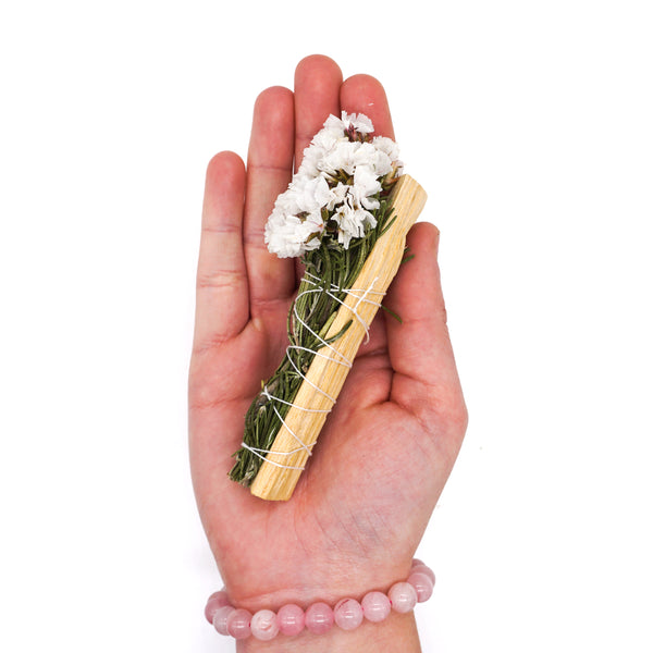 Faiza Natural's smudge stick of palo santo, lavender, rosemary, cinnamon, and white sinuata, bound with twine; side profile on hand.